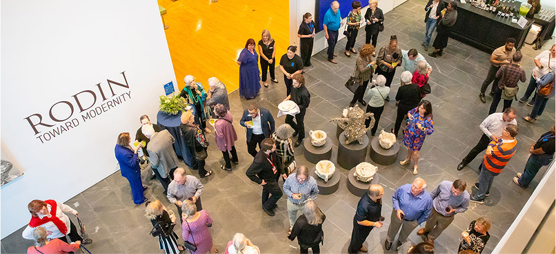 A crowd gathers at the Rodin: Toward Modernity exhibition, mingling and admiring sculptures on pedestals in a spacious, well-lit gallery—a true highlight among Louisiana museums and perfect for a Lafayette family friendly outing.