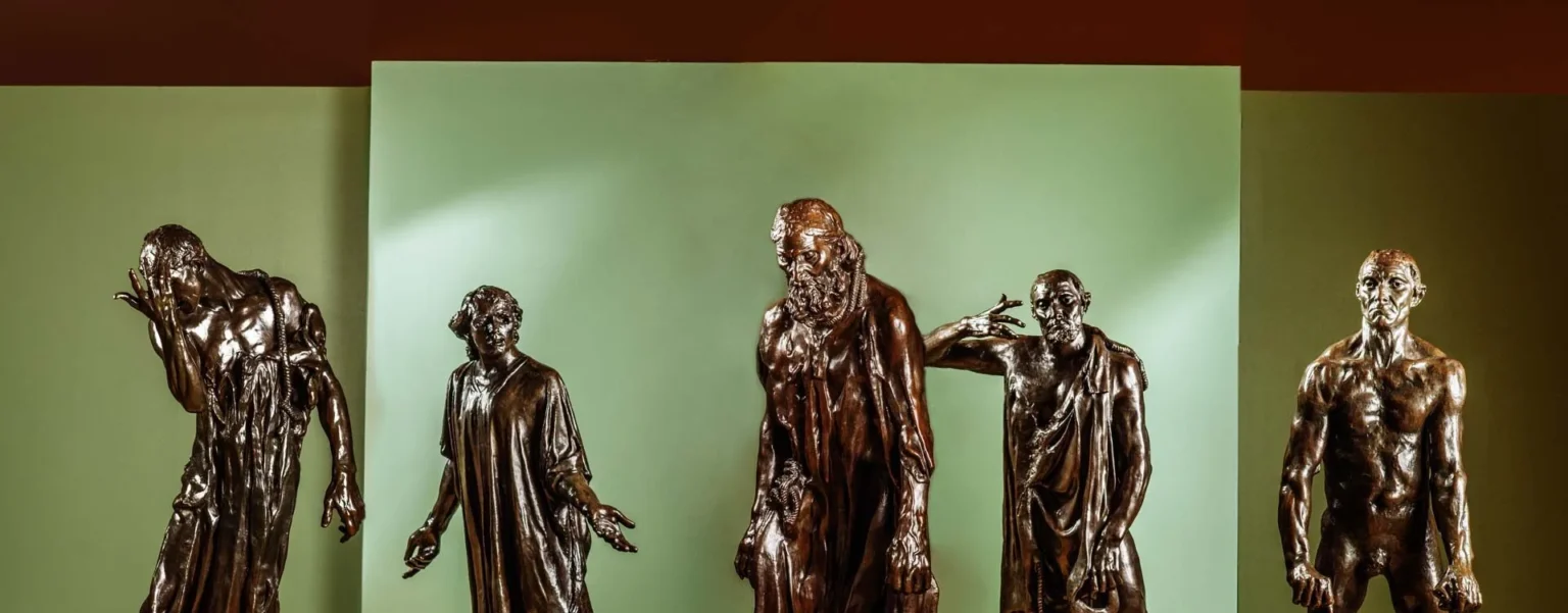 Five bronze statues of standing figures in dramatic poses are displayed against a light green background with a brown top border, highlighting expressive gestures and varied clothing—showcasing the creativity found at the Hilliard Art Museum.