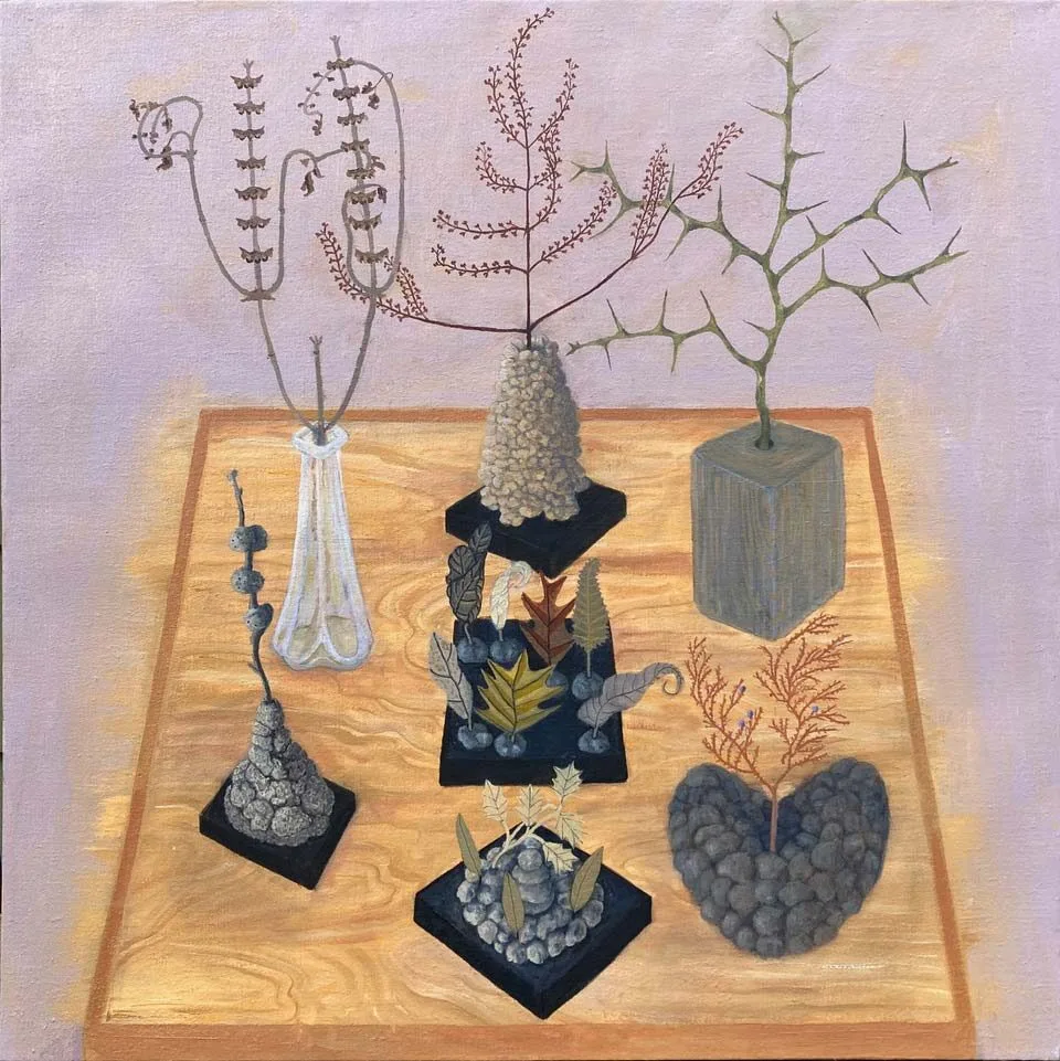 A wooden table displays seven arrangements of dried plants and stones, each uniquely shaped and placed on small black platforms; the background is a muted lavender color.