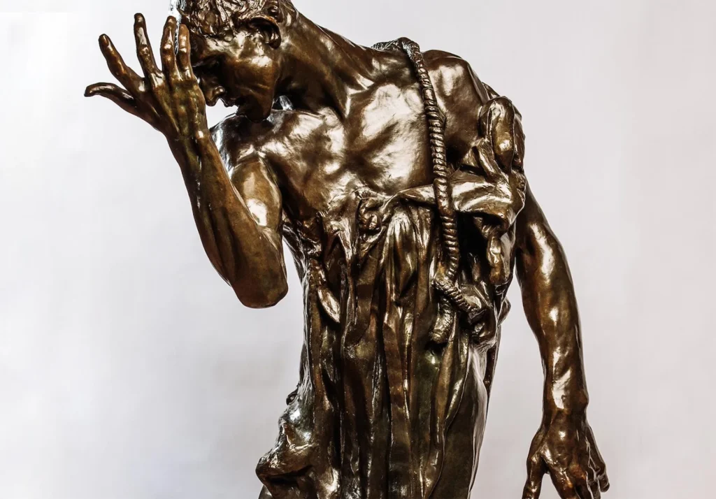 Bronze statue by Brisco of a standing man with his head bowed, one hand raised to his face, and a rope draped around his neck and shoulder, set against a plain light background.