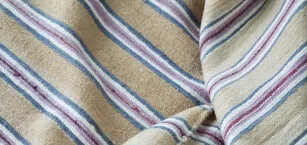 Beige fabric with a textured surface, featuring horizontal stripes in blue, purple, and white. The material appears to be slightly wrinkled or folded.