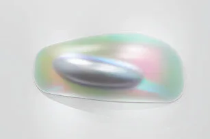 A smooth, oval-shaped metallic object rests on an iridescent, reflective surface displaying soft pastel colors against a plain light background.