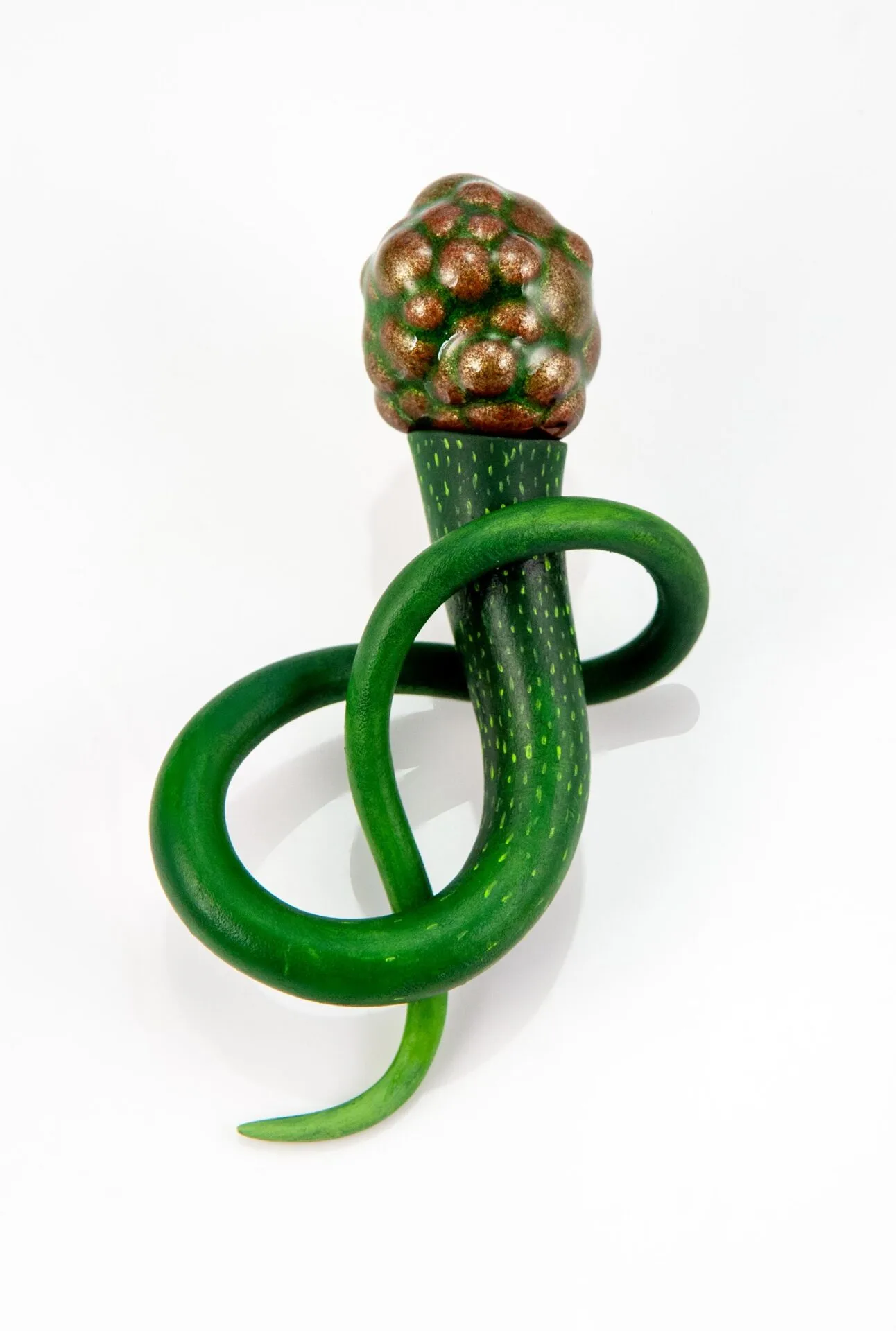 A sculpture by Mare Martin resembling a twisting green plant stem with small yellow dots, ending in a bulbous, textured, bronze-colored top, displayed on a white background.