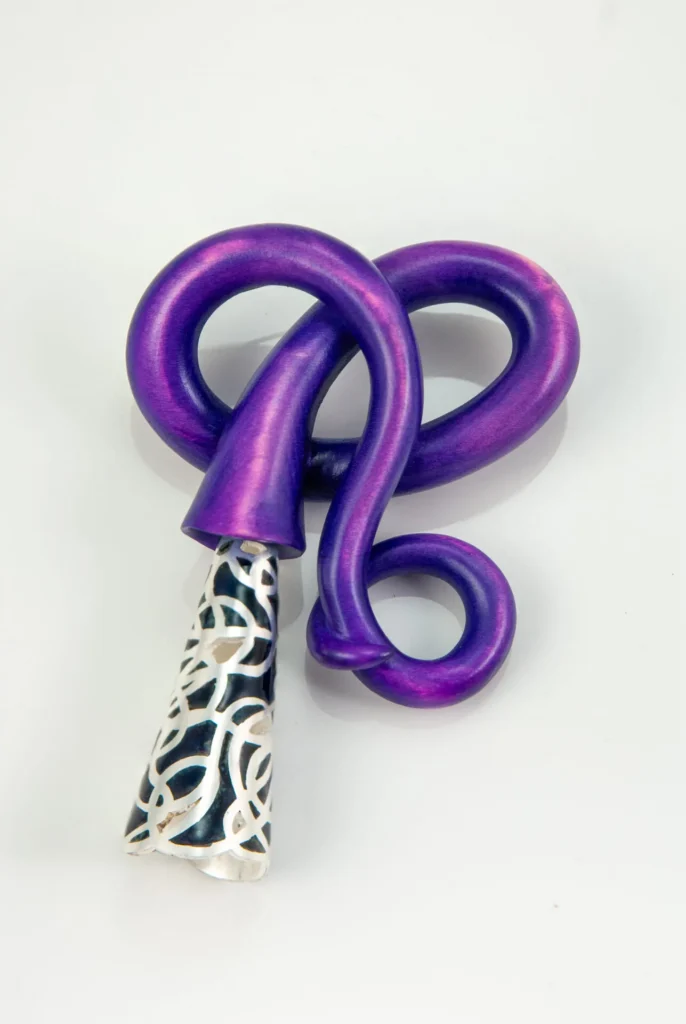 A sculptural object by Mare Martin with bold, curved loops in metallic purple and a conical end featuring an intricate black and white lattice pattern, displayed on a light gray background.