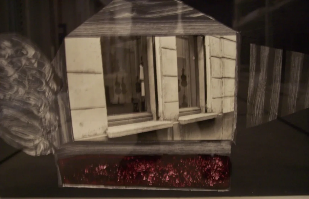 A black and white photo of an open window in a building with light shutters. The window is framed by a transparent overlay shaped like a house, with a red textured area at the bottom.