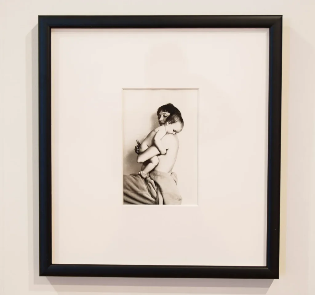 Black and white photo of two people embracing, displayed in a black frame on a white wall. The photo is centered with a wide white mat surrounding it.