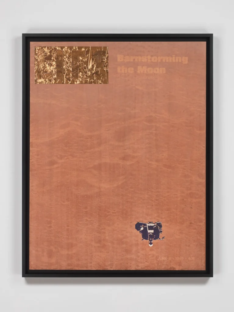 A framed artwork with a reddish-brown background, gold-foil text Barnstorming the Moon at the top right, and a small, dark object resembling a lunar lander at the bottom right.
