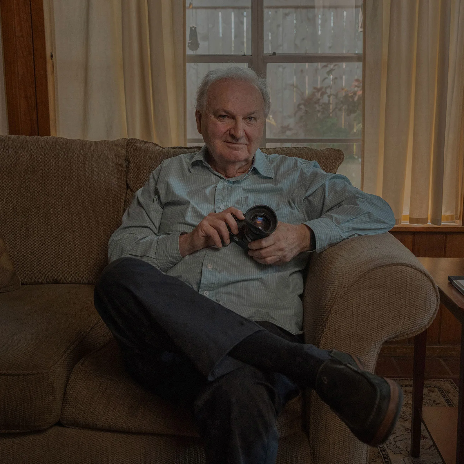 An older man sitting on a sofa, holding a camera lens.
